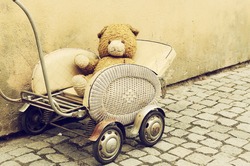 Old dirty Teddy bear toy sitting in the retro baby carriage on the street - lost lonely children concept, vintage hipster grunge image