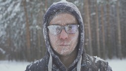 a frozen man with glasses in the snow looks at the camera in the winter forest after a snow storm