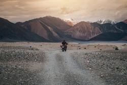Tourist riding an adventure motorcycle on tuff and bumpy road on rock mountain in sunset lightning to explore the world, with copy space 