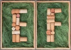 Alphabet letter E and  F made of  wine corks on green background in wooden box. ABC set  