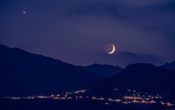 Half moon is rising up on a purple horizon, Mountains and lights from villages