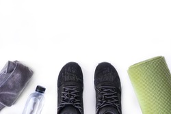 Top view of fitness accessories on white background with copy space, black sneaker, bottle, towel and green yoga mat
