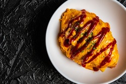 Omelette rice with tomato ketchup on a white plate against a black design board.