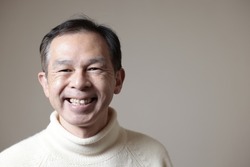 Middle-aged Asian man in white turtleneck wool sweater under gray background. Concept image of Warm Biz, stability in daily life, and sustainable living.