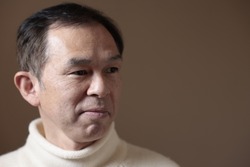 Middle-aged Asian man in white turtleneck wool sweater under gray background. Concept image of Warm Biz, stability in daily life, and sustainable living.