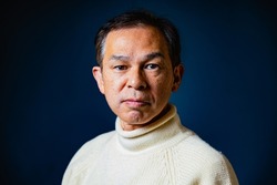 Middle-aged Asian man in white turtleneck wool sweater under dark blue background. Concept image of Warm Biz, stability in daily life, and sustainable living.