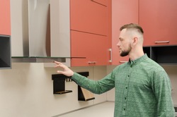 Attractive bearded man in a green shirt turns on a fume hood in a modern kitchen.