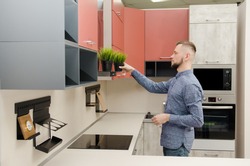 attractive bearded man puts a decorative pot with artificial grass on a fume hood in a modern kitchen.