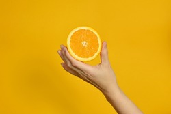 The girl's hand holds a cut round slice of fresh tropical orange. An orange in a woman's hand on a yellow background is isolated. Orange slice. The girl gently holds a citrus in one hand