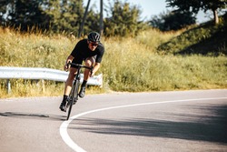 Mature bearded cyclist in sport outfit and protective helmet riding bicycle on fresh air. Sportsman leading active lifestyle with green nature around.