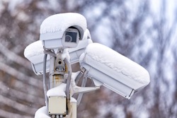 city street outdoor surveillance CCTV camera on stand exterior closeup view with white snow cap cold season winter blurred background