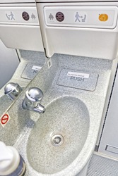 airplane toilet room interior with bathroom sink closeup vertical view of aircraft air travel water closet wc equipment including mirror faucet soap bottle return to seat sign modern plane cabin