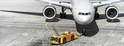 airplane on airport runway with pushback tractor attached to plane nose gear aerial top front view passenger jet engine aircraft towing by ground vehicle to terminal gate black and white wide banner