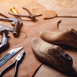 Leather craft tools on wooden background. Workplace for shoemaker. Piece of leather. Cobbler workplace with tools, leather and shoes last. Small shoemaker workplace with tools