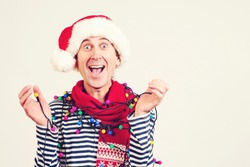 Happy excited man in Santa hat, with garlands on him. Handsome guy celebrated New Year. Winter holidays and christmas. Christmas sales, celebration and fashion concept.