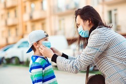 Coronavirus outbreak. Mother puts her son a face protective mask outdoors. Stop the coronavirus spreading. Quarantine. Protective measures. Public crowded place. People prevent infection from virus.