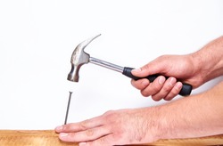Hammer in hand hammering a nail into a wooden Board on an isolated white background.