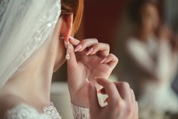 Wedding earrings on a woman's hand, she takes earrings, bride fees, morning bride, white dress, wearing earrings