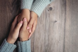 Two people holding hands together with love and warmth on wooden table