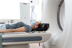 A woman in a medical mask lies on the tomograph table. woman is undergoing computed axial tomography examination in a modern hospital