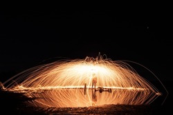 Wide landscape long exposure shot of man spinning glowing steel wool producing light trails. Night photography. Reflection on water surface.