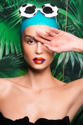 Portrait of beautiful woman with colorful make up, beauty magazine editorial ready, Caucasian girl, with swimming hat, sunglasses and tropical exotic background