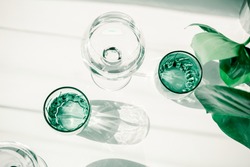 Glasses of water on white table. Harsh light through glasses, shadows. Clean minimalist contemporary art. Conceptual image. Green and white clean colors. Pure water in glass. Simple visual concept.