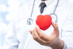 Professional medical doctor holding a red heart ball on blur office in the hospital and bokeh background. Concept of health care.