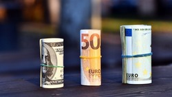 Three rolls of European (Euro) currency bills in 50 Euro and 100 Euro bills and $1,000 in 100 dollar bills rolled up with a rubber band. Concept of savings in $ and €