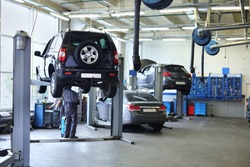 Three black cars stand in small service station and two men repair one car.
