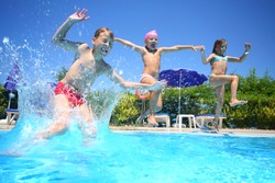 Two little girls and boy fun jumping into the swimming pool, shot through the underwater package.