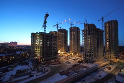 Seven high buildings under construction with cranes at evening