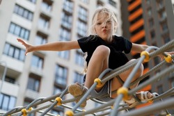 Girl child climbed to the top of the alpine grid on the playground.