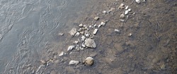 The riverbed is covered in small rocks and pebbles. The water is shallow and clear, and you can see the rocks through the water.
