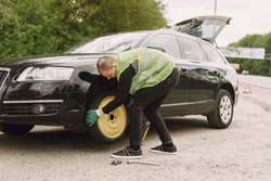 Worker changes a broken wheel of a car. The driver should replace the old wheel with a spare. Man changing wheel after a car breakdown.