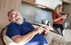 elderly man with a smartphone sitting in a home chair.