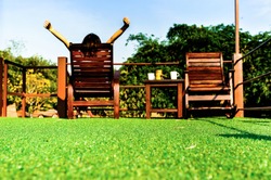 happy woman feel comfortable and relaxing on wooden sun bed furniture outdoor on green artificial grass and looking the blue sky background, coffee morning concept