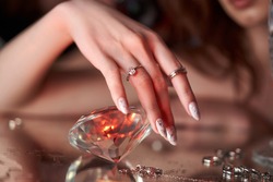 Beauty Woman holds big diamond in hand while lying on table. Beautiful hands, professional manicure, large brilliant