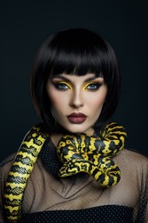 Beauty woman short haircut python yellow snake on her neck. A yellow snake on the shoulders of a girl. Beauty yellow eye shadow makeup, dark burgundy lipstick