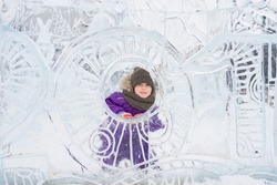 Boy hiding behind an ice sculpture. Patterned wall of ice. Winter park