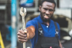 Portrait of attractive African man smiling to the camera and big wrench tools in hand. Expertise mechanic working in automobile repair garage. 
