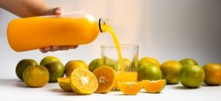 Closeup fat woman hand pouring fresh orange juice into glass. Glass with fresh orange juice and sliced orange in white background