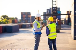 Two caucasian man engineer worker wearing hardhat safety helmet and vest working in  logistic shipping yard. Marine and carrier insurance concept. Cargo container yard.
