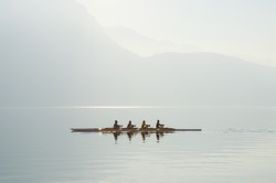 Four rowers on boat floating on sunny morning on background of mountains on lake of Lugano. Concept of healthy lifestyle, water sports. Switzerland.