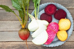Four different varieties of organic beets on a gray metal plate. Plain red beetroot, striped chioggia, white and yellow on a wooden background.
