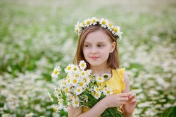 Portrait of a girl in a yellow T-shirt on a blooming field of daisies with a bouquet in her hands and a wreath on her head. A field of daisies on a summer day. Selective focus.