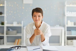 Portrait of confident happy young lady, professional coach, course author, successful business woman or female psychologist, sitting in her home office at desk with open notebook looking at camera