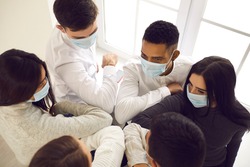 High angle group of diverse business people bumping elbows instead of handshake during coronavirus pandemic. From above mixed-race coworkers wearing face masks greeting each other during flu epidemic