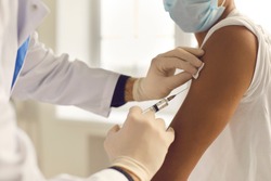 Doctor in medical gloves giving Covid-19, AIDS or flu antivirus vaccine shot to African-American patient. Close-up of hands holding syringe and cleaning skin on upper arm before antiviral injection