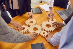 Cropped shot of team of company employees joining cogwheels on office table as metaphor for perfectly working business system, finding best solutions, collaboration, effective teamwork and management
